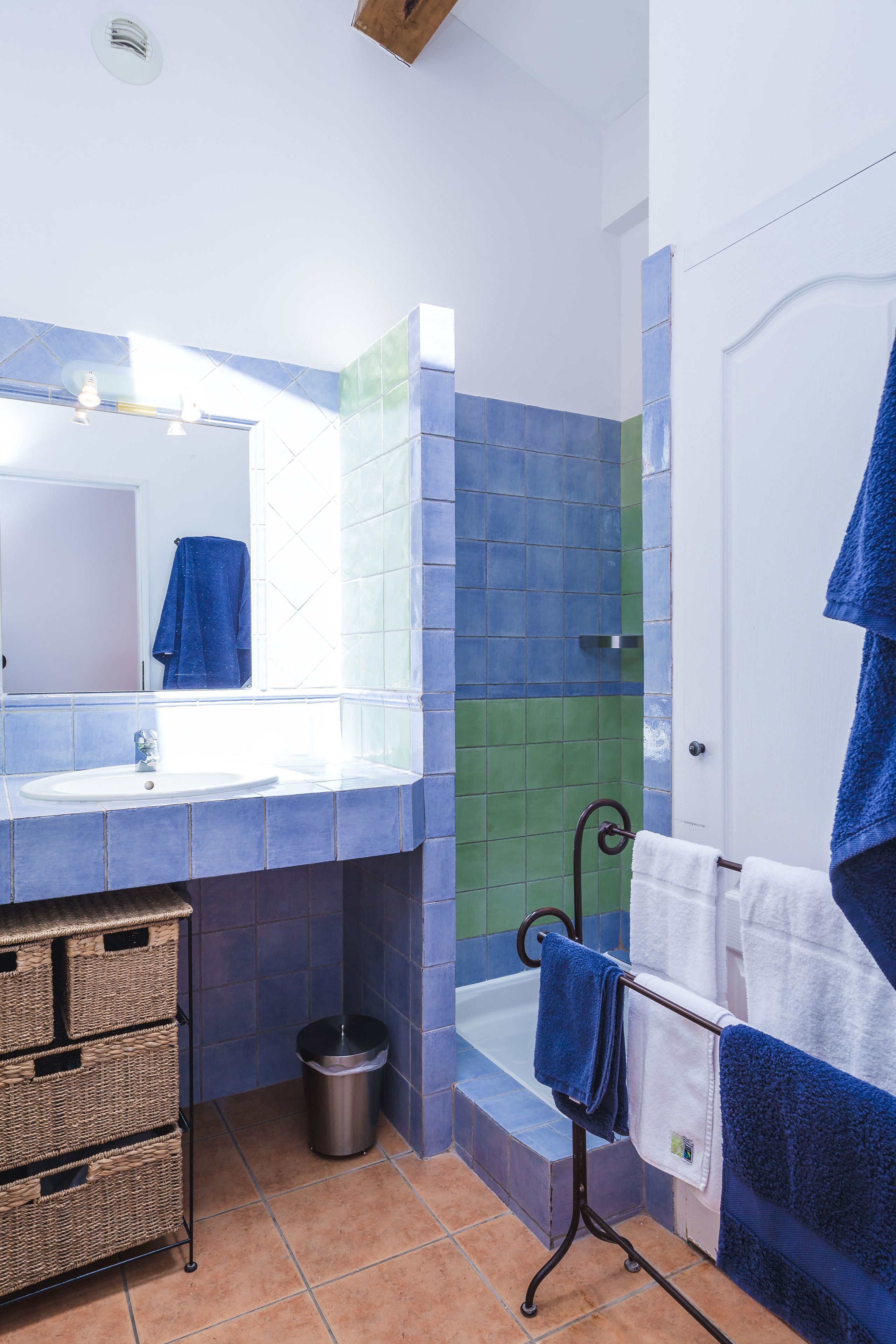 A bathroom with a sink, mirror, and bathtub. There are blue and green tiles on the walls, and a blue towel hanging on a rack.