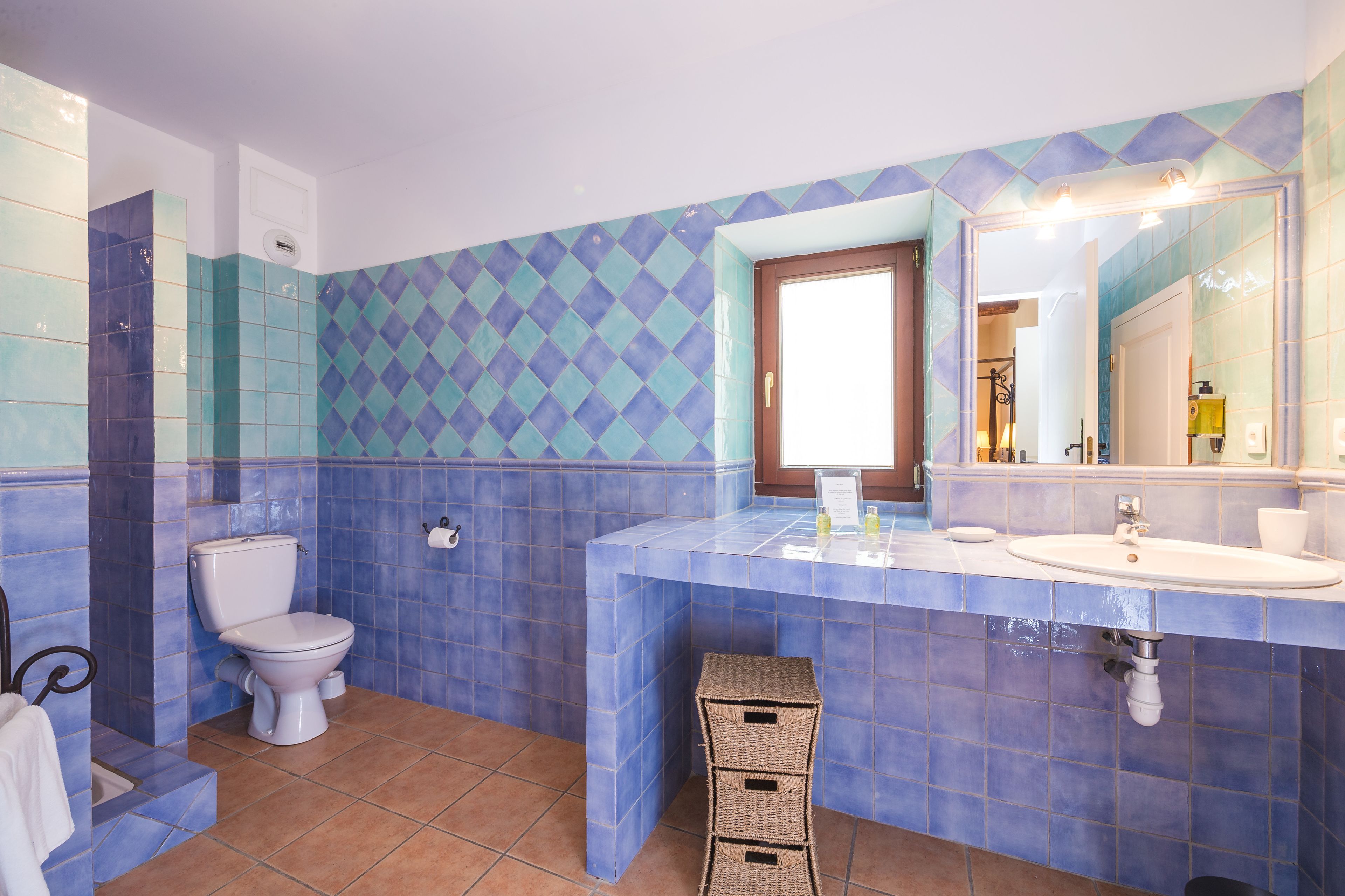Ein Badezimmer mit blauen und weißen Fliesen, einer Toilette, einem Waschbecken und einem Spiegel.