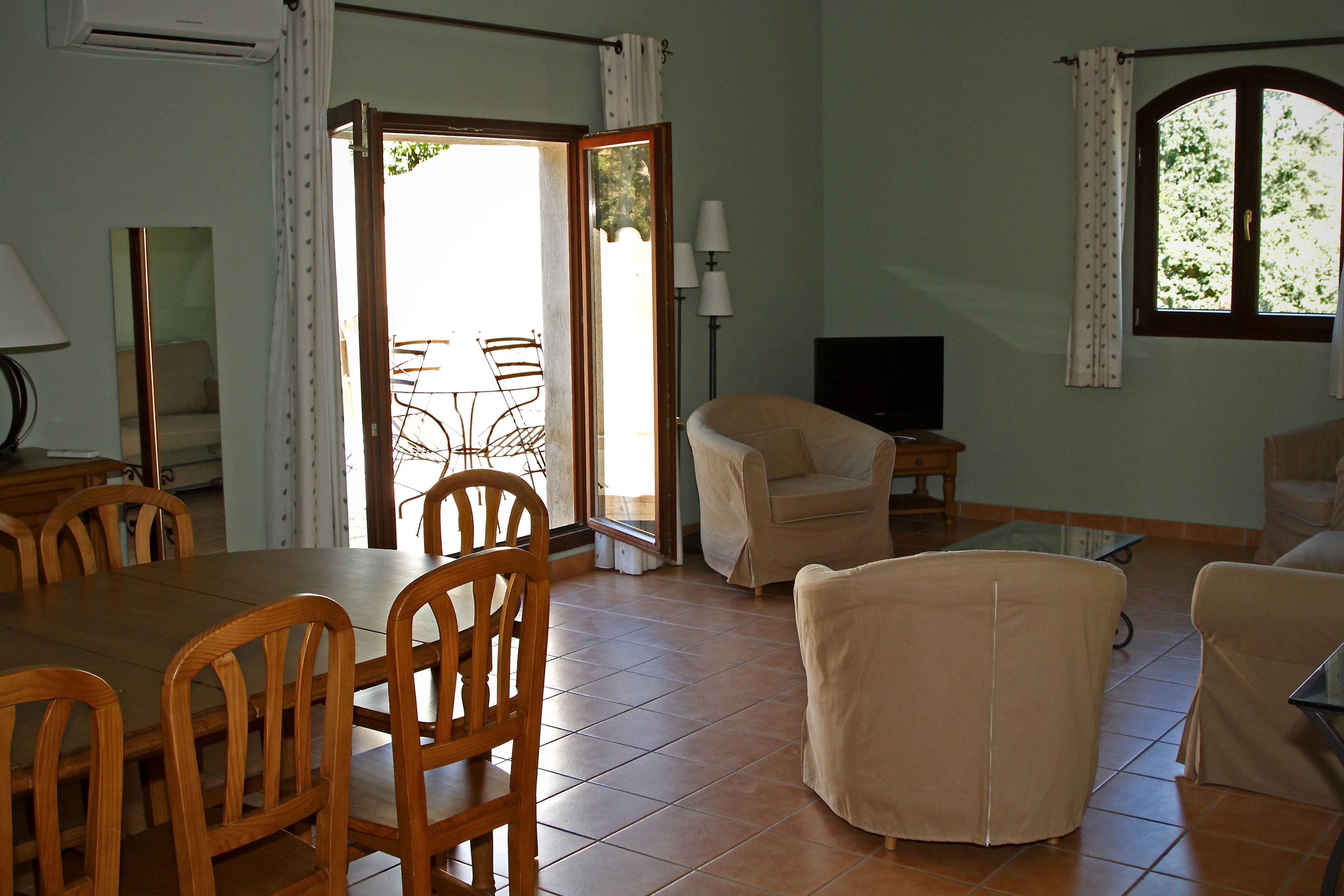 A dining area with a wooden table and chairs, a sofa, a TV, and a window with curtains.