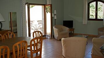 A dining area with a wooden table and chairs, a sofa, a TV, and a window with curtains.
