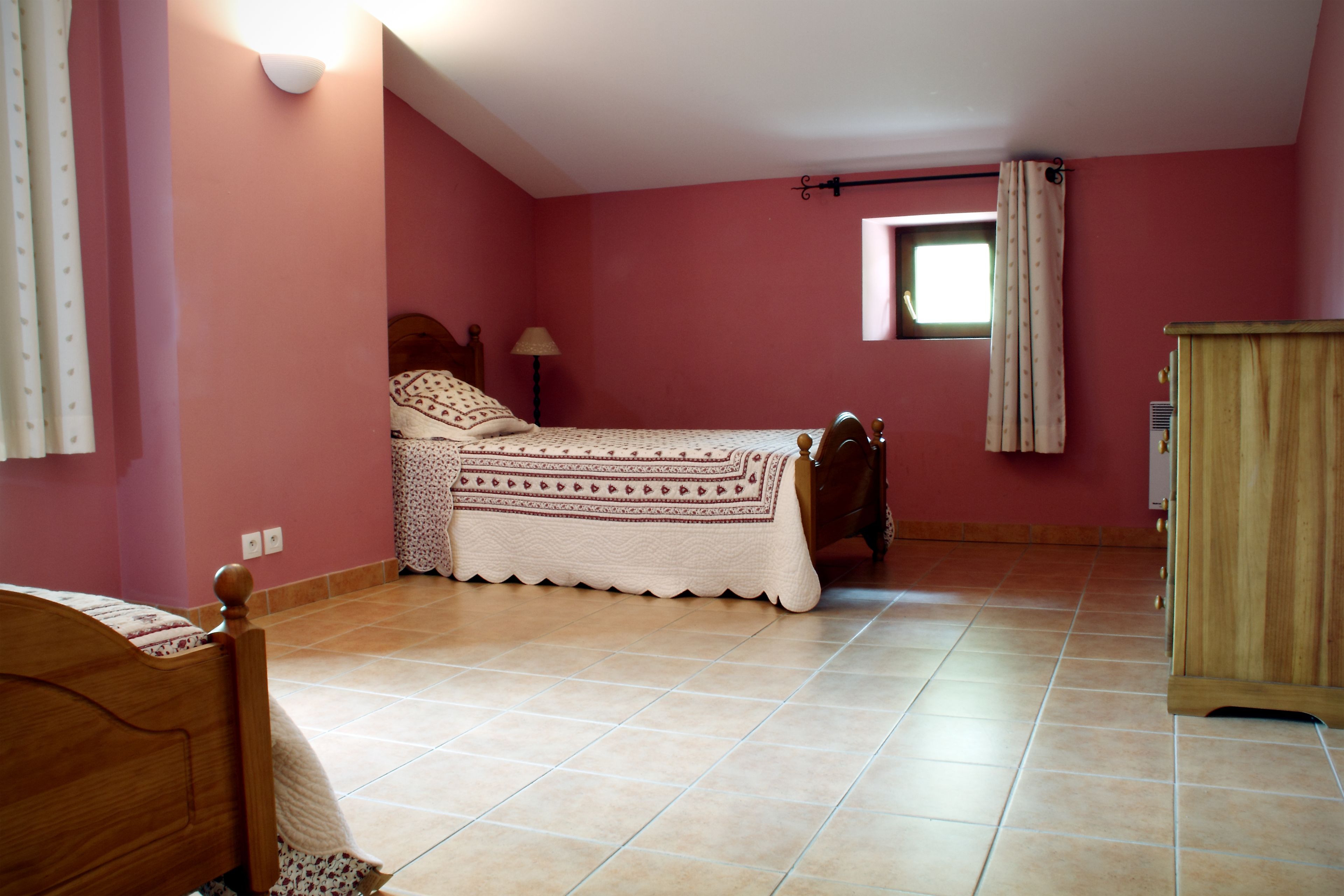 Une chambre à coucher avec un lit, une armoire en bois, une fenêtre avec des rideaux et une lampe.
