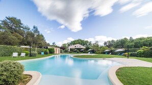 A swimming pool with a curved edge, surrounded by well-maintained grass and hedges. There are lounge chairs and umbrellas in the background, suggesting outdoor seating areas. - Le Relais du Grand Logis Cadarache ITER (Mirabeau)