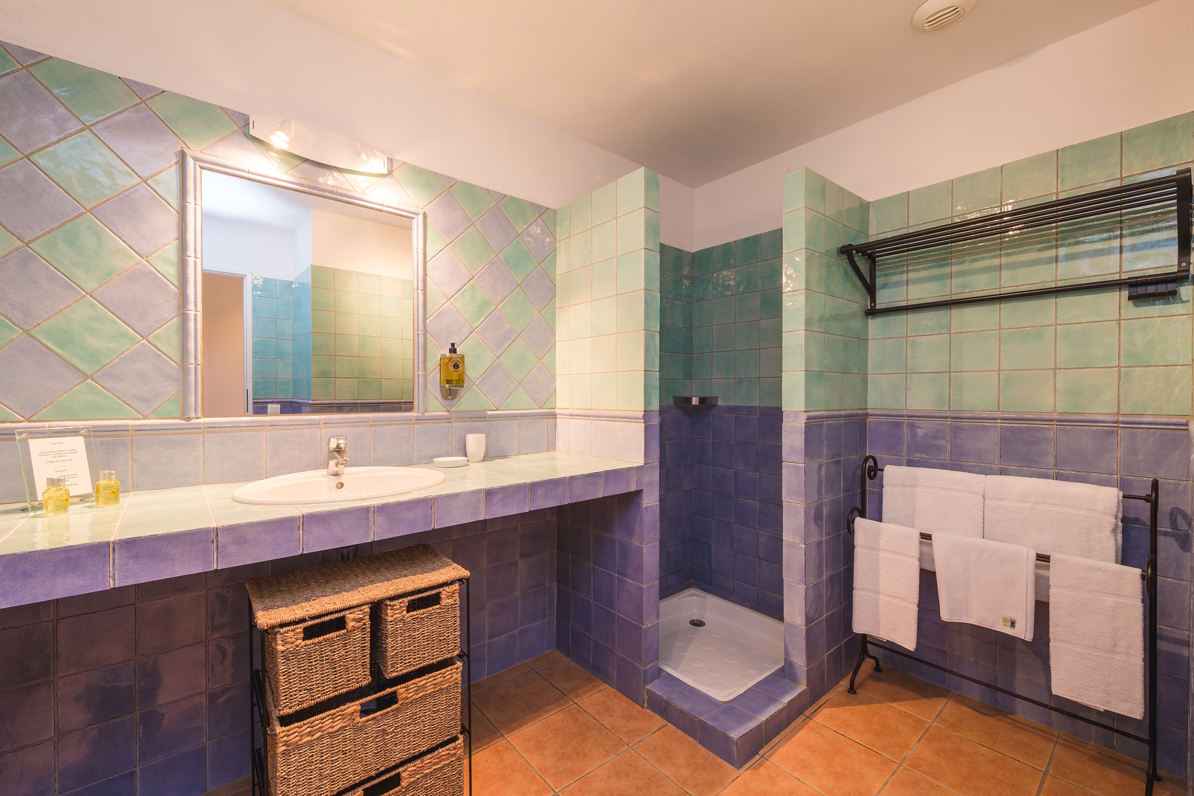 A bathroom with a sink, mirror, shower, and towel rack.