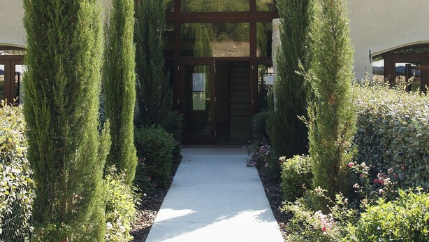 A pathway leading to a building with a wooden pergola entrance, surrounded by neatly trimmed hedges and flowering plants. - Le Relais du Grand Logis Cadarache ITER (Mirabeau)