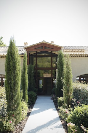 A pathway leading to a building with a wooden pergola entrance, surrounded by neatly trimmed hedges and flowering plants. - Le Relais du Grand Logis Cadarache ITER (Mirabeau)