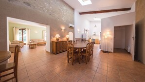 A spacious living area with a dining table, chairs, and a kitchen in the background. - Le Relais du Grand Logis Cadarache ITER (Mirabeau)
