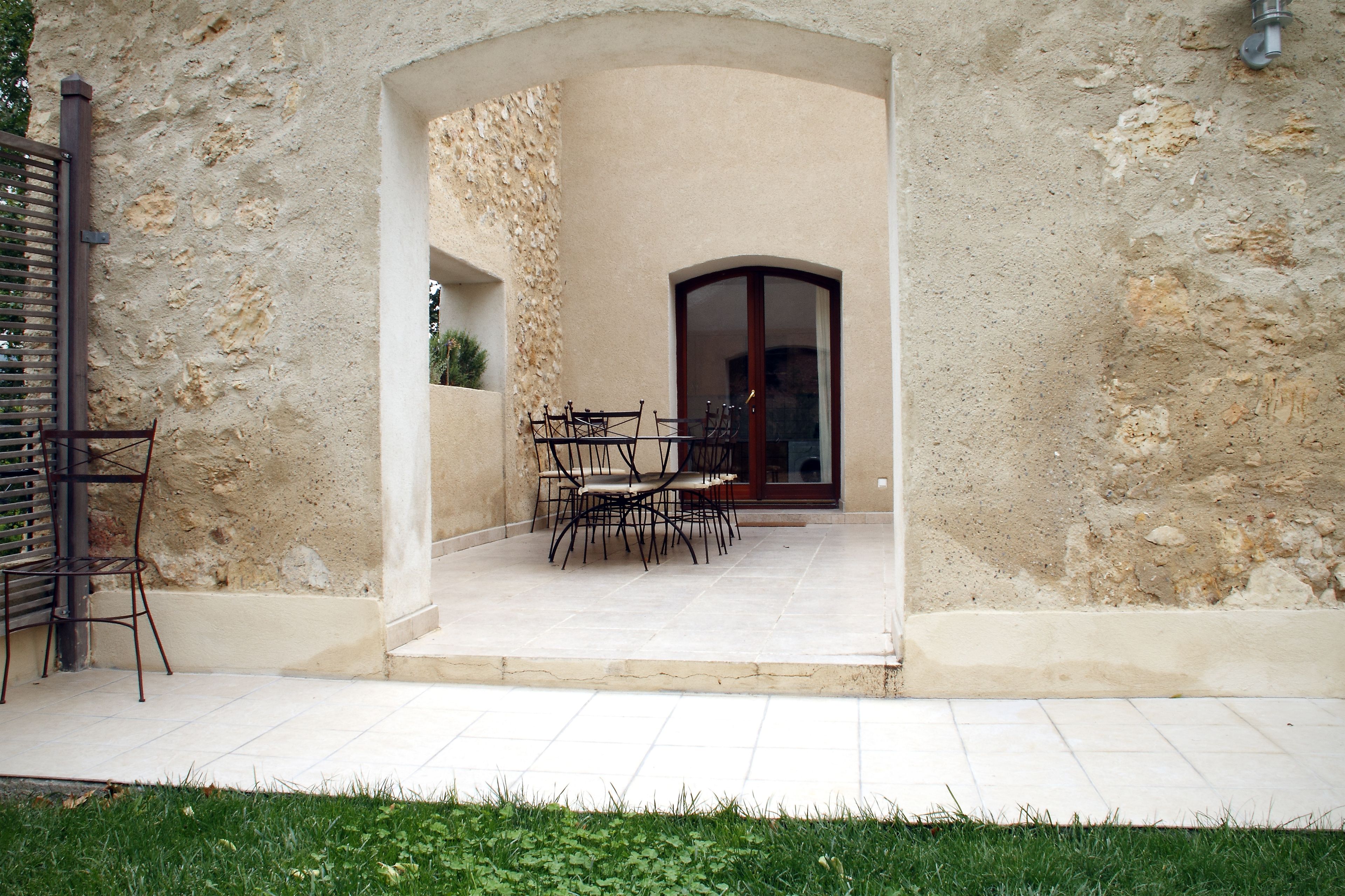 An outdoor patio with a stone wall, a wooden door, and a table with chairs.