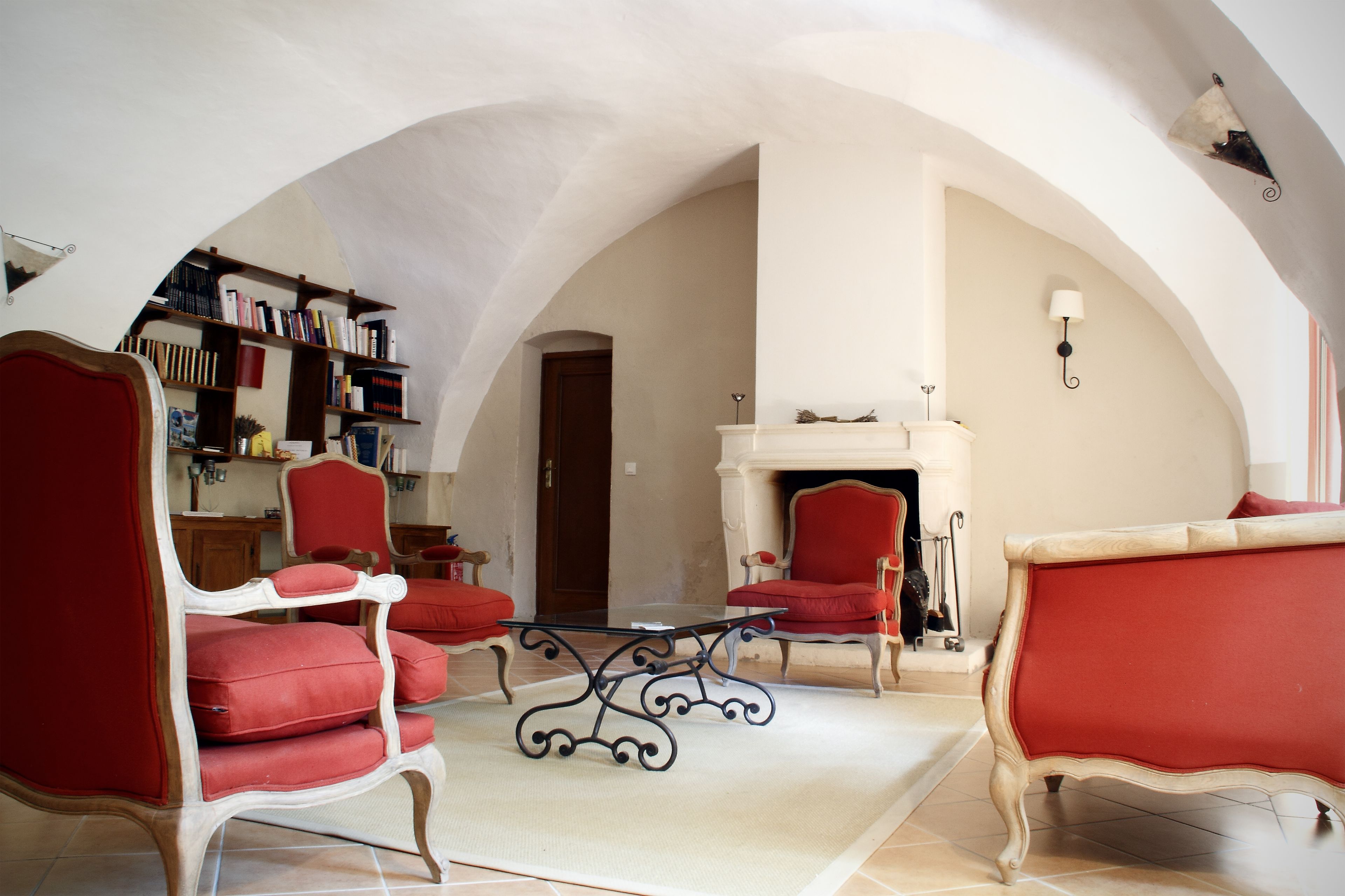 Una habitación con chimenea, sillones tapizados en rojo, una mesa de centro y una estantería.