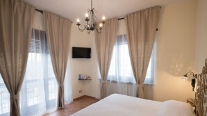 A bedroom with a large bed, curtains, a chandelier, a TV, and a radiator.