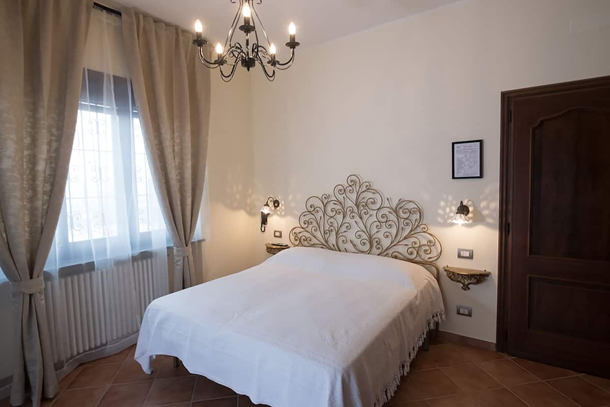 Een slaapkamer met een groot bed, een kroonluchter, wandlampen, een radiator en een houten deur.