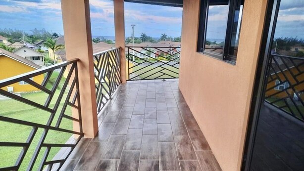 Un balcón con suelo de baldosas y barandillas de metal, con vistas a una zona residencial.