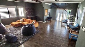 Amplia sala de estar con un sofá seccional grande, un sillón de peluche negro y una mesita. Una escalera conduce a un nivel superior.