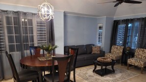 Una sala de estar con una mesa redonda de madera, sillas oscuras, un sofá, sillones estampados, una mesa de centro y un ventilador de techo.