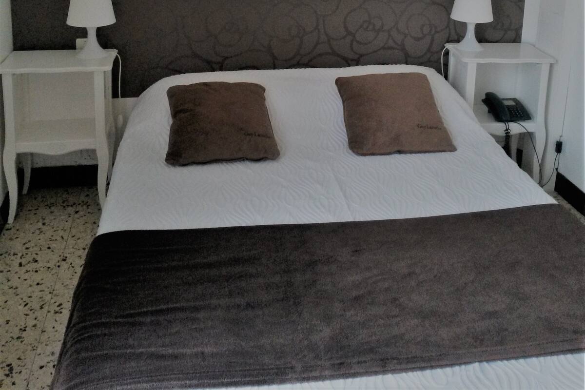 Ein Hotelzimmer mit einem großen Bett, zwei Nachttischen mit Lampen, einem gerahmten Kunstwerk über dem Bett und einer Wand mit Muster.