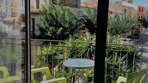 Un balcón con sillas verdes y una mesita, con vista a una calle con edificios y una torre.