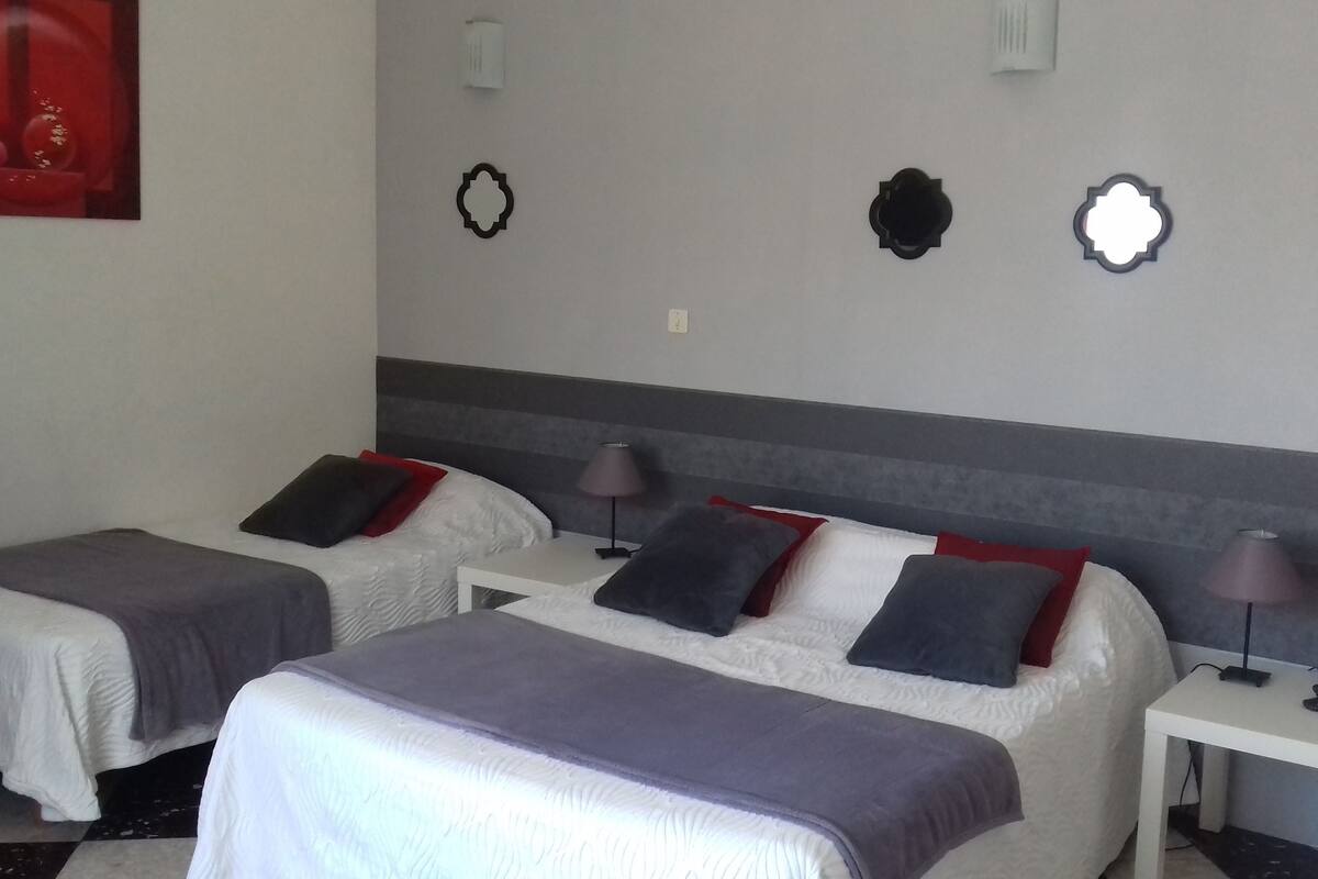 Ein Hotelzimmer mit zwei Betten, jeweils mit Kopfkissen und Decke. An den Nachttischen stehen Lampen und ein Telefon. Das Zimmer hat ein schlichtes Design mit grau-weißer Farbgebung.