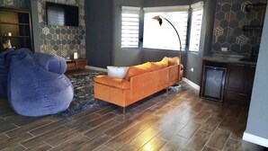 Un salon avec un canapé, un fauteuil poire, un téléviseur et une fenêtre avec des stores.
