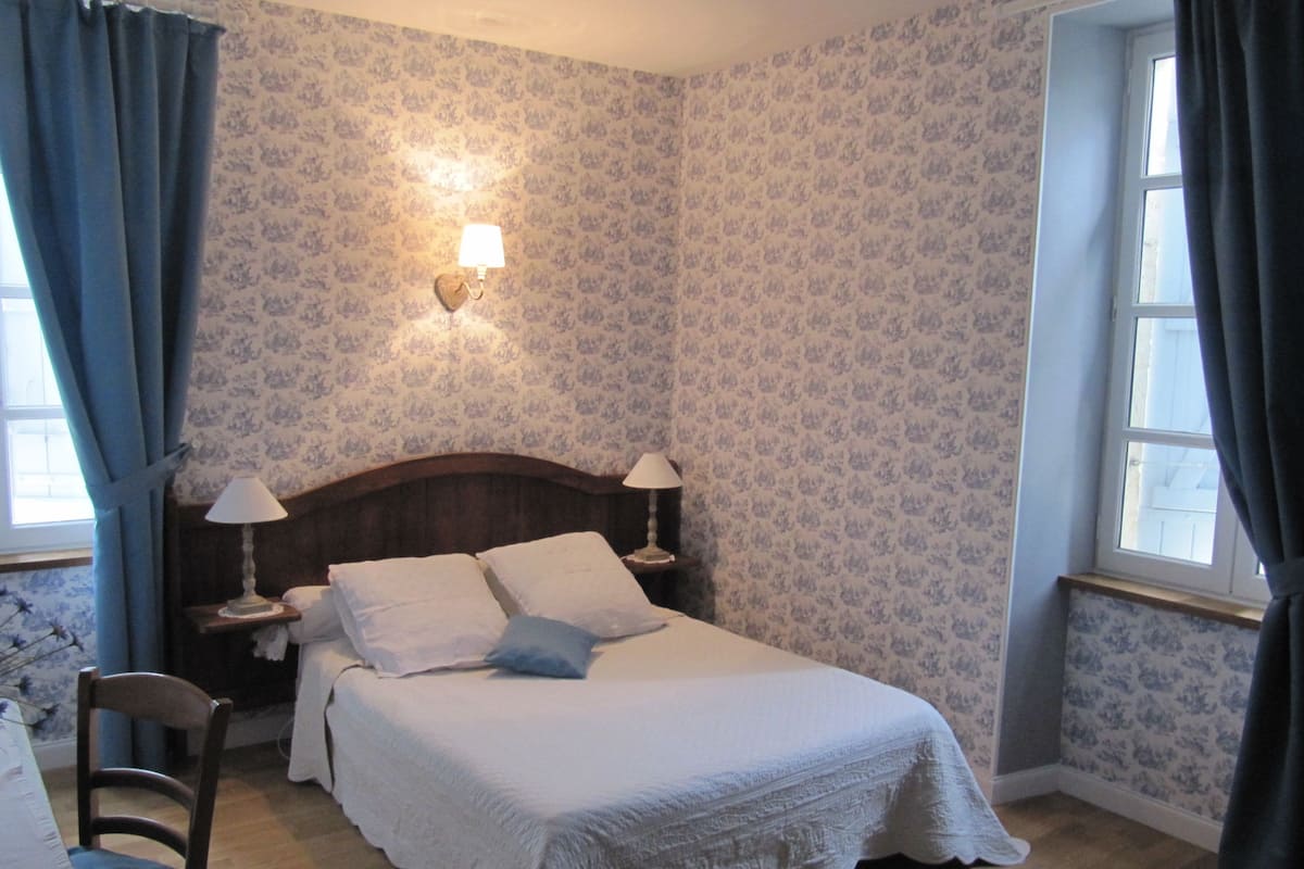 Une chambre à coucher avec un lit, deux tables de chevet avec des lampes, une chaise et une fenêtre avec des rideaux.