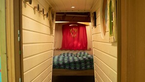 Un couloir étroit mène à une pièce où se trouve un lit superposé, des murs en bois et un rideau rouge.