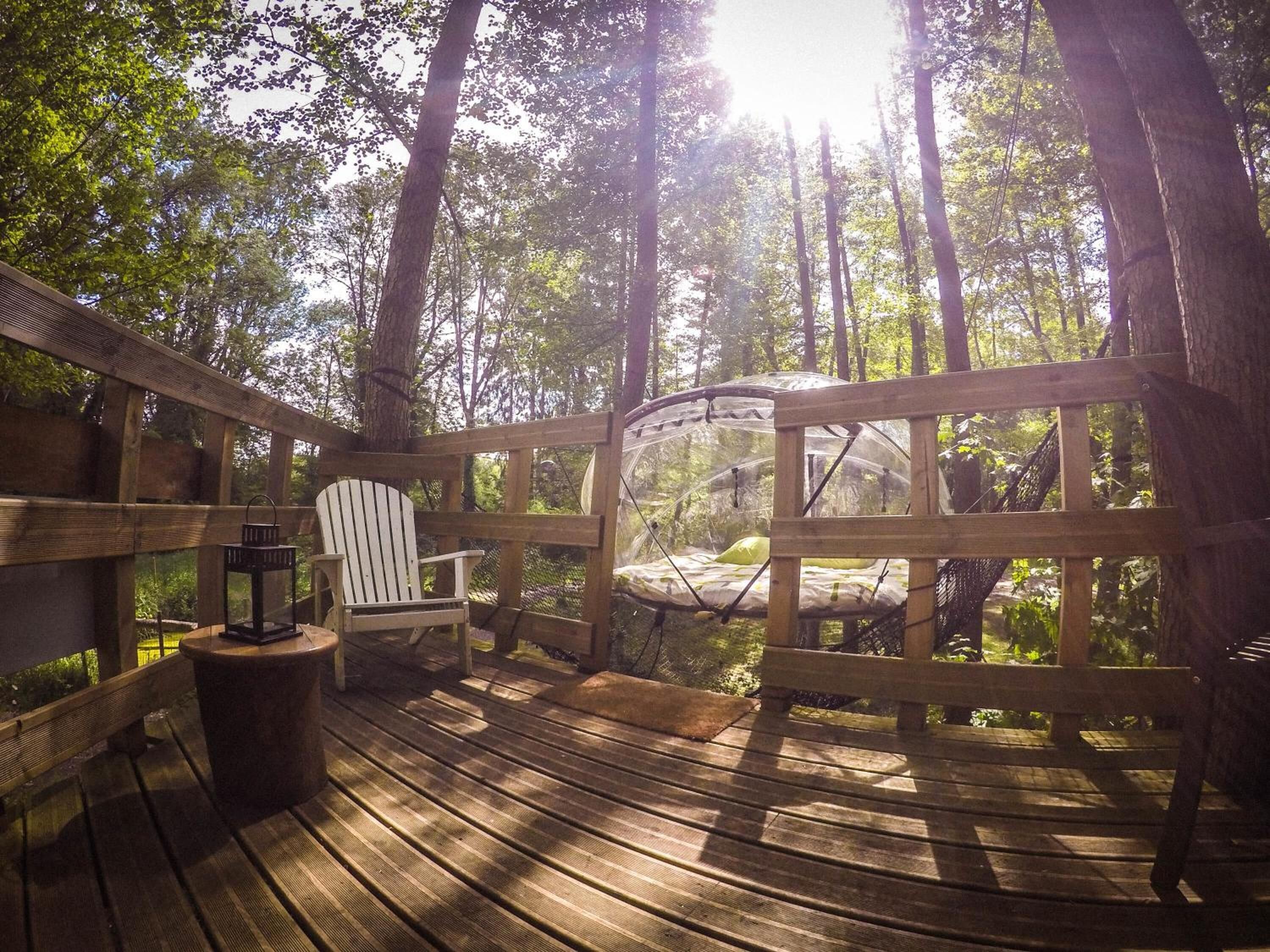 Puinen terassi, jossa on läpinäkyvällä lasikupolilla varustettu tuoli, valkoinen Adirondack-tyylinen tuoli ja lyhty.