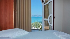 Une chambre à coucher avec un lit, une fenêtre avec des rideaux et une vue sur la mer.