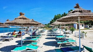 Une plage bordée de rangées de chaises longues et d’ombrelles en chaume, dont certaines sont occupées.