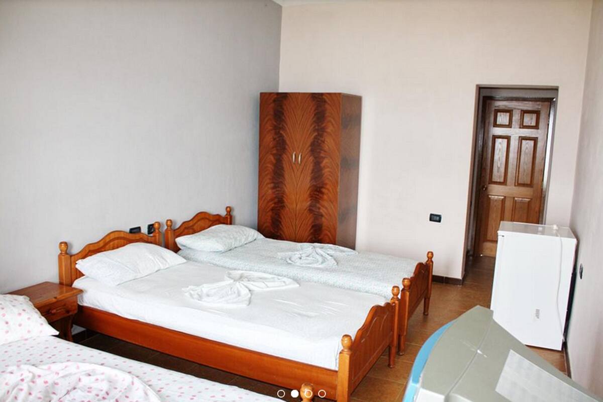 A bedroom with a wooden bed, a wardrobe, a door, and a refrigerator.