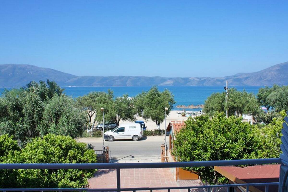A view of a coastal area with a white van parked in the foreground, trees, and a clear blue sky.