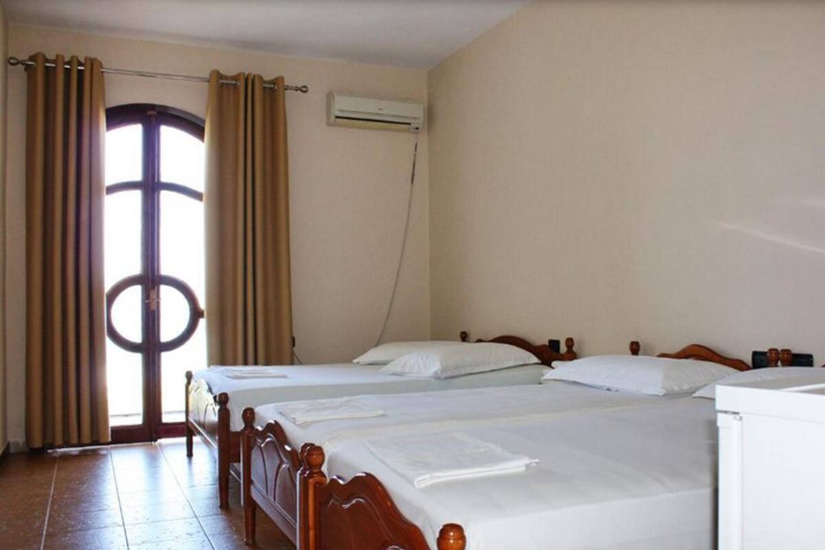 A hotel room with two beds, a window with curtains, an air conditioning unit, and a tiled floor.