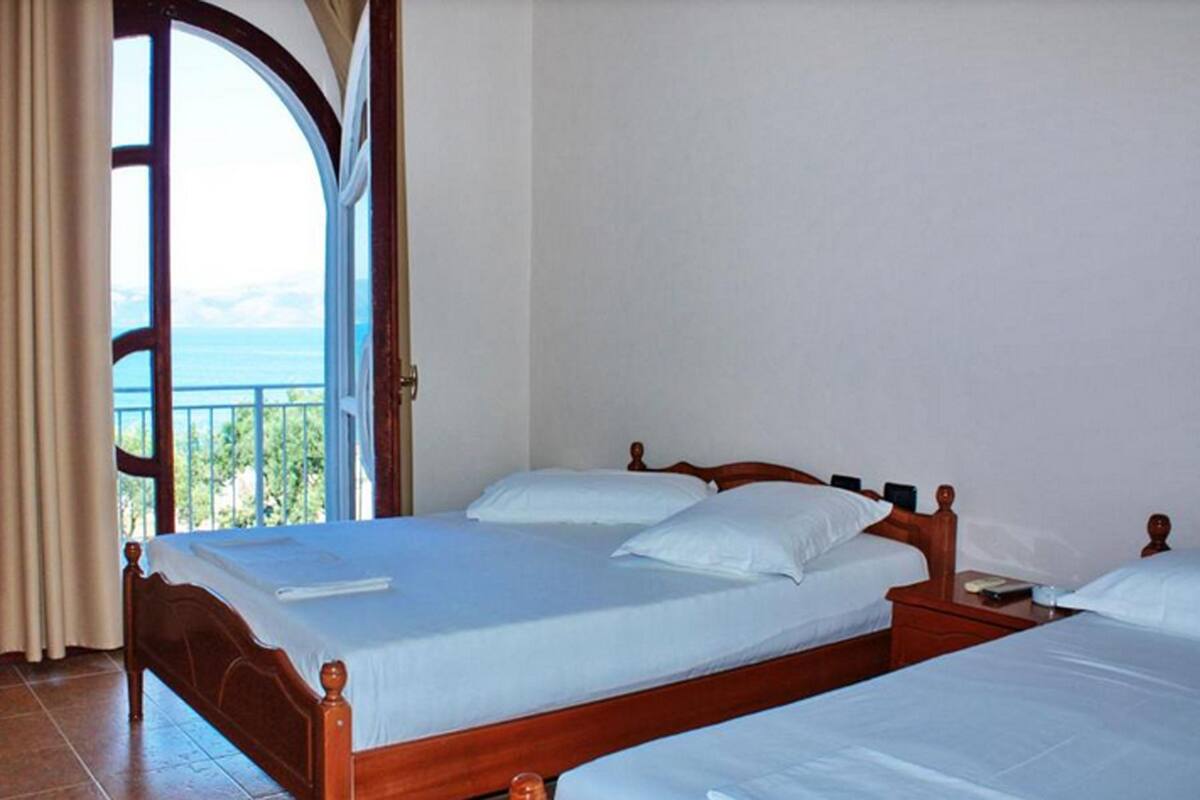 A bedroom with two wooden beds, a large window with a view of the sea, and a balcony.