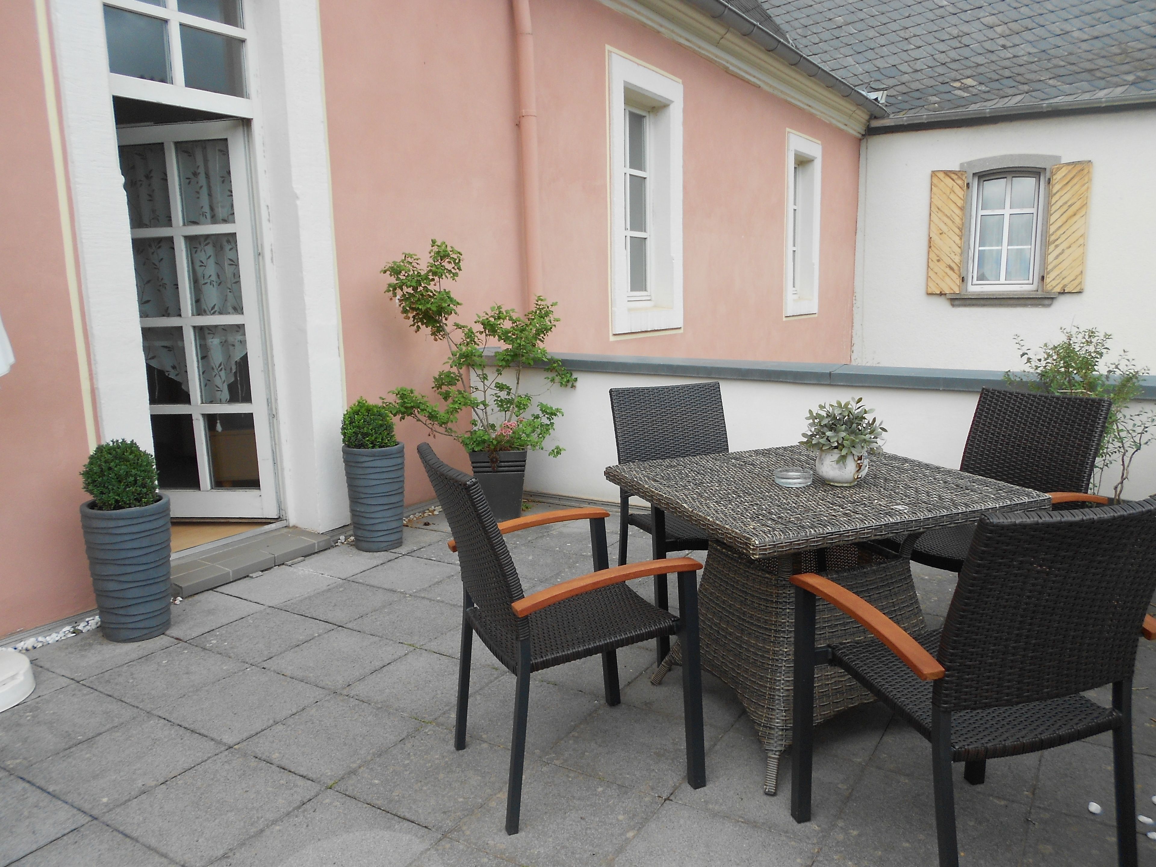 A patio with a table and chairs, potted plants, and a building with a pink wall and windows.