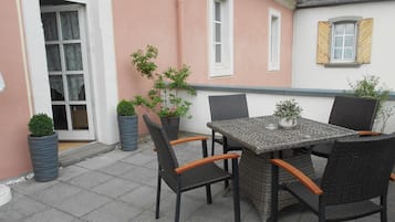 A patio with a table and chairs, potted plants, and a building with a pink wall and windows.