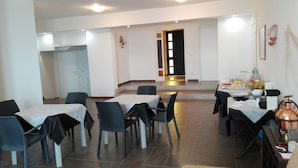 A dining area with multiple tables and chairs, a kitchen area with a stove and sink, and a door leading to another room. - La nave sul mare di Taormina B&B (Letojanni)