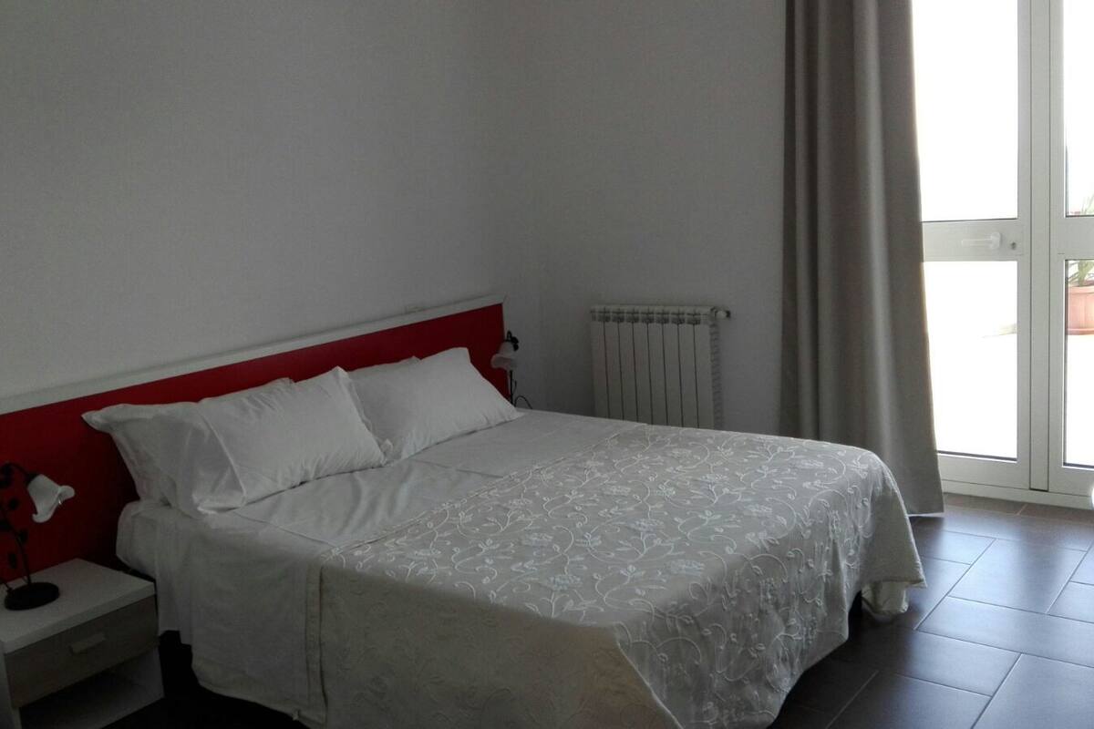 Un dormitorio con cama, mesita de noche, lámpara y ventana con cortinas.