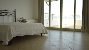 A bedroom with a bed, a nightstand, a lamp, and a view of a balcony through a large window. - La nave sul mare di Taormina B&B (Letojanni)