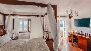 A bedroom with a four-poster bed, a desk with a chair, a television, and a view of the outdoors. - Dom Dinis Marvão (Marvao)
