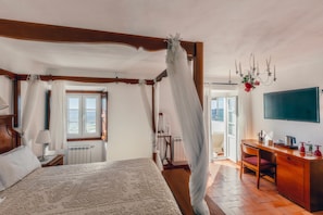 Ein Schlafzimmer mit Himmelbett, Schreibtisch mit Stuhl, Fernseher und Blick ins Freie.