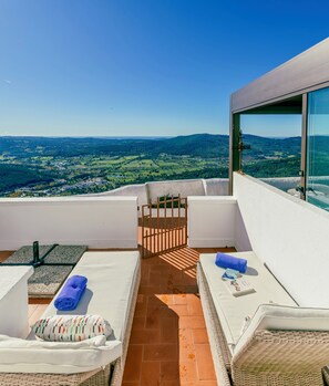 Ein Balkon mit Blick auf eine grüne Landschaft, ein Stuhl und zwei Liegestühle mit Handtüchern.