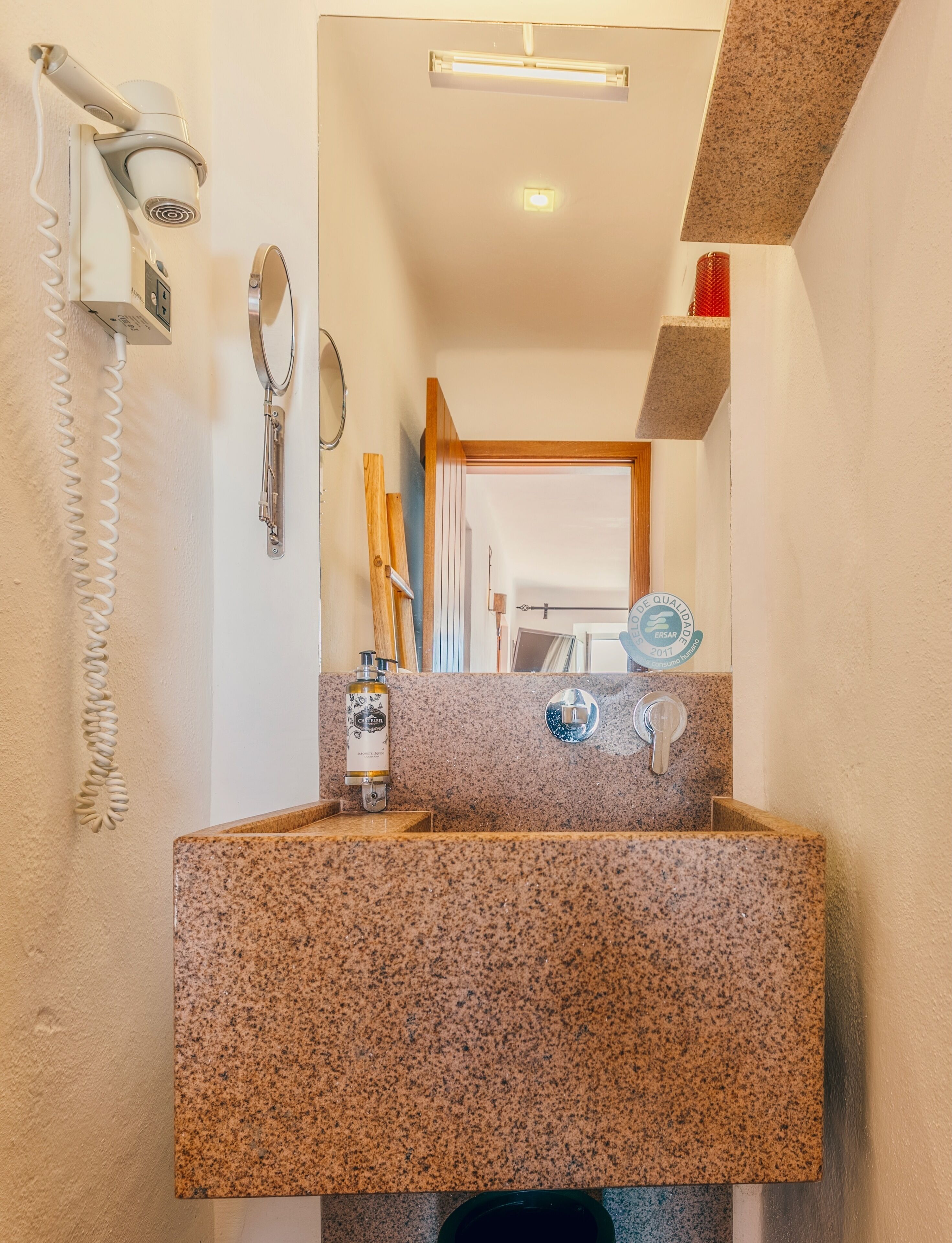 Ein Badezimmer mit Marmorwaschbecken, einem Fön, einem Spiegel und einer Handseifenflasche.