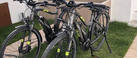 Varias bicicletas estacionadas en un césped, con un muro blanco y un banco al fondo.