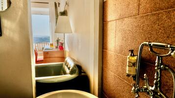 A bathroom with a bathtub, a sink, a mirror, and a window with a view.