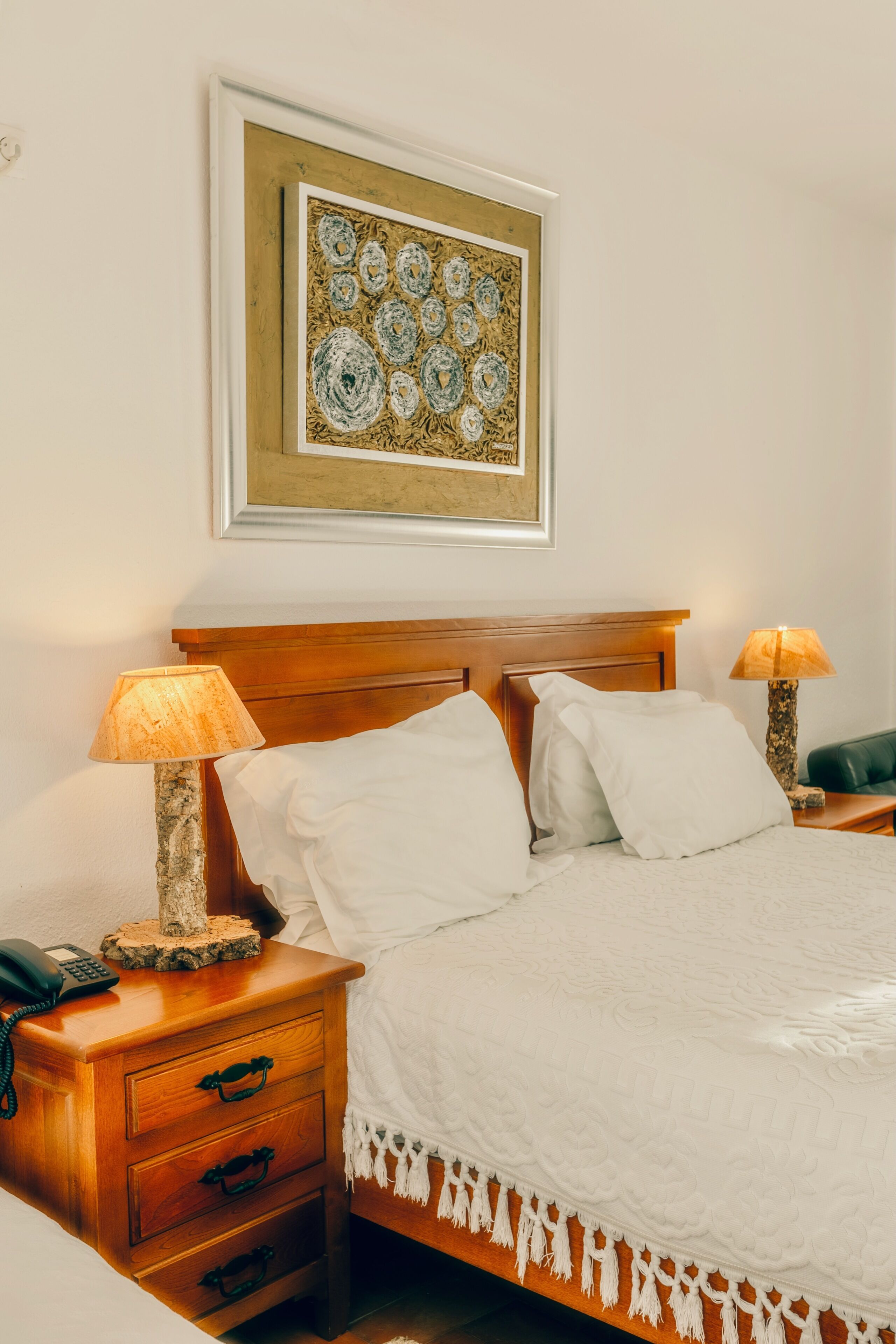 A neatly made bed with white linens, a wooden headboard, and a framed artwork above. There are two bedside tables with lamps and a telephone.