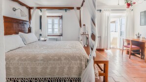 A bedroom with a large bed, wooden headboard, and a canopy. There is a desk and chair in the room, and a view of the outdoors through a window. - Dom Dinis Marvão (Marvao)