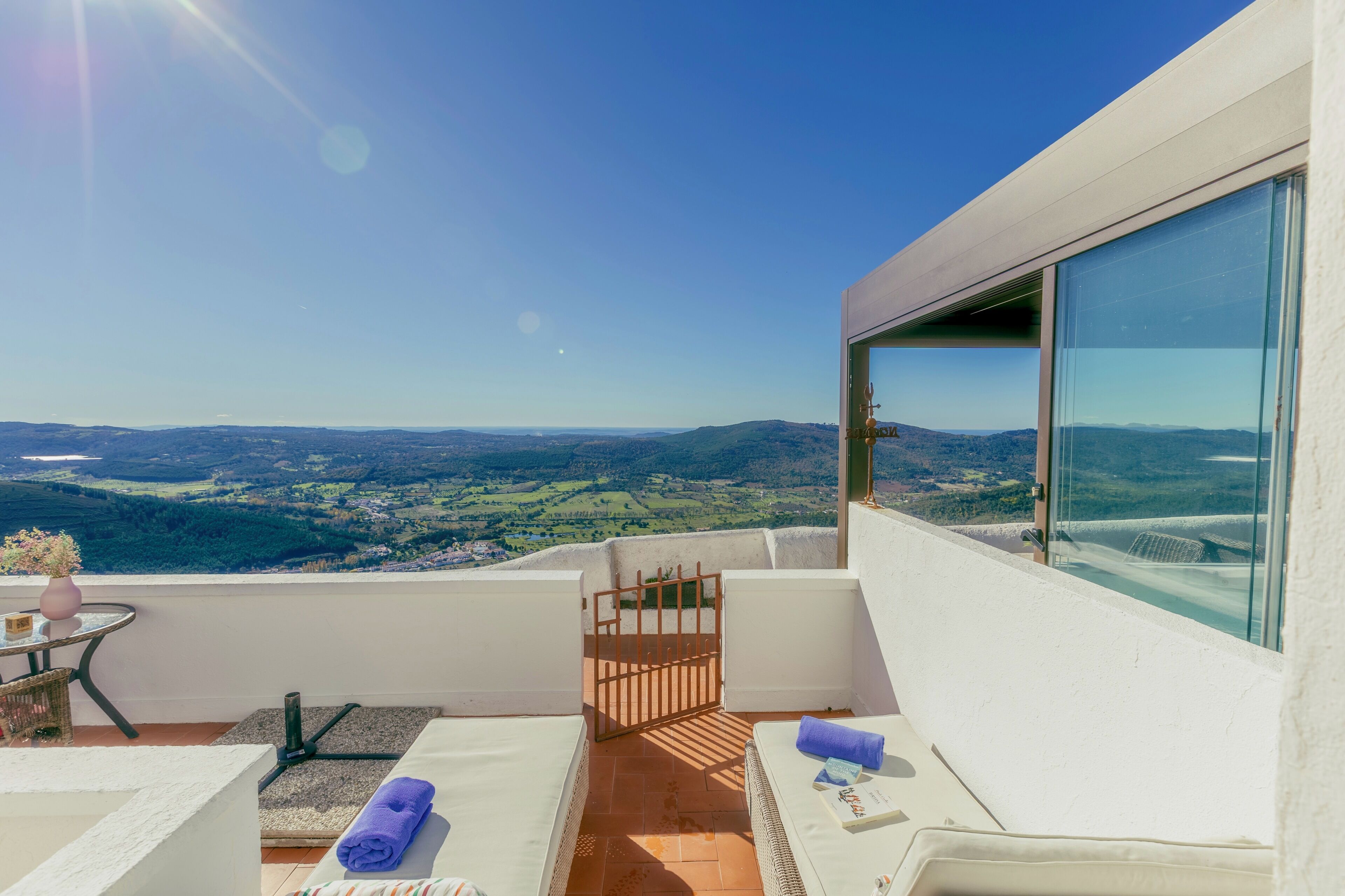A balcony with a view of a valley, a table with a vase, and a chair.