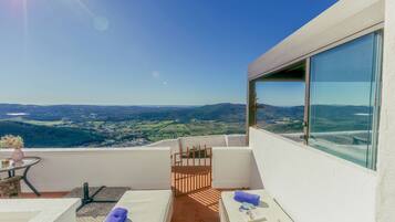 A balcony with a view of a valley, a table with a vase, and a chair.
