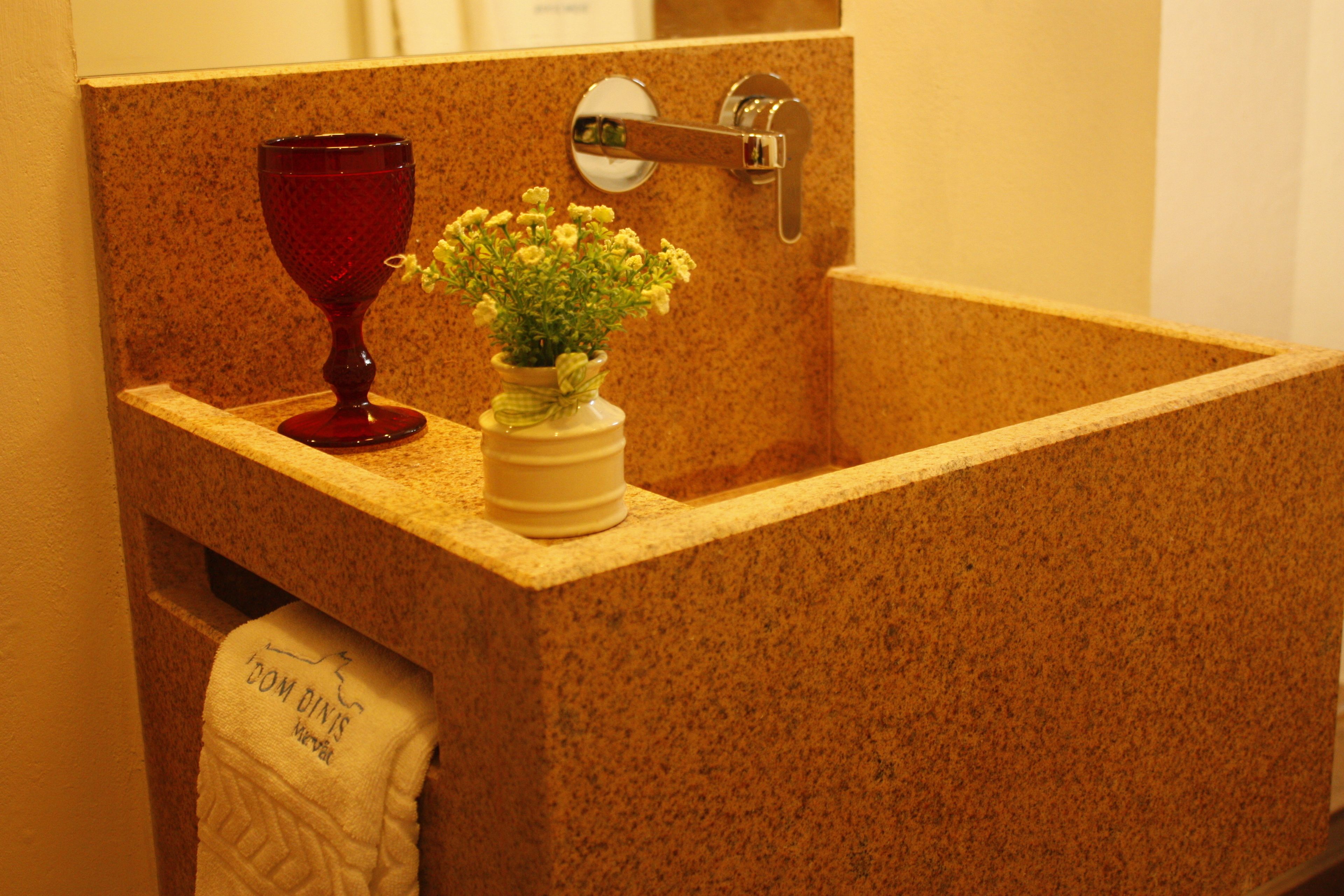 Un baño con encimera de granito, un vaso rojo y un florero con flores.