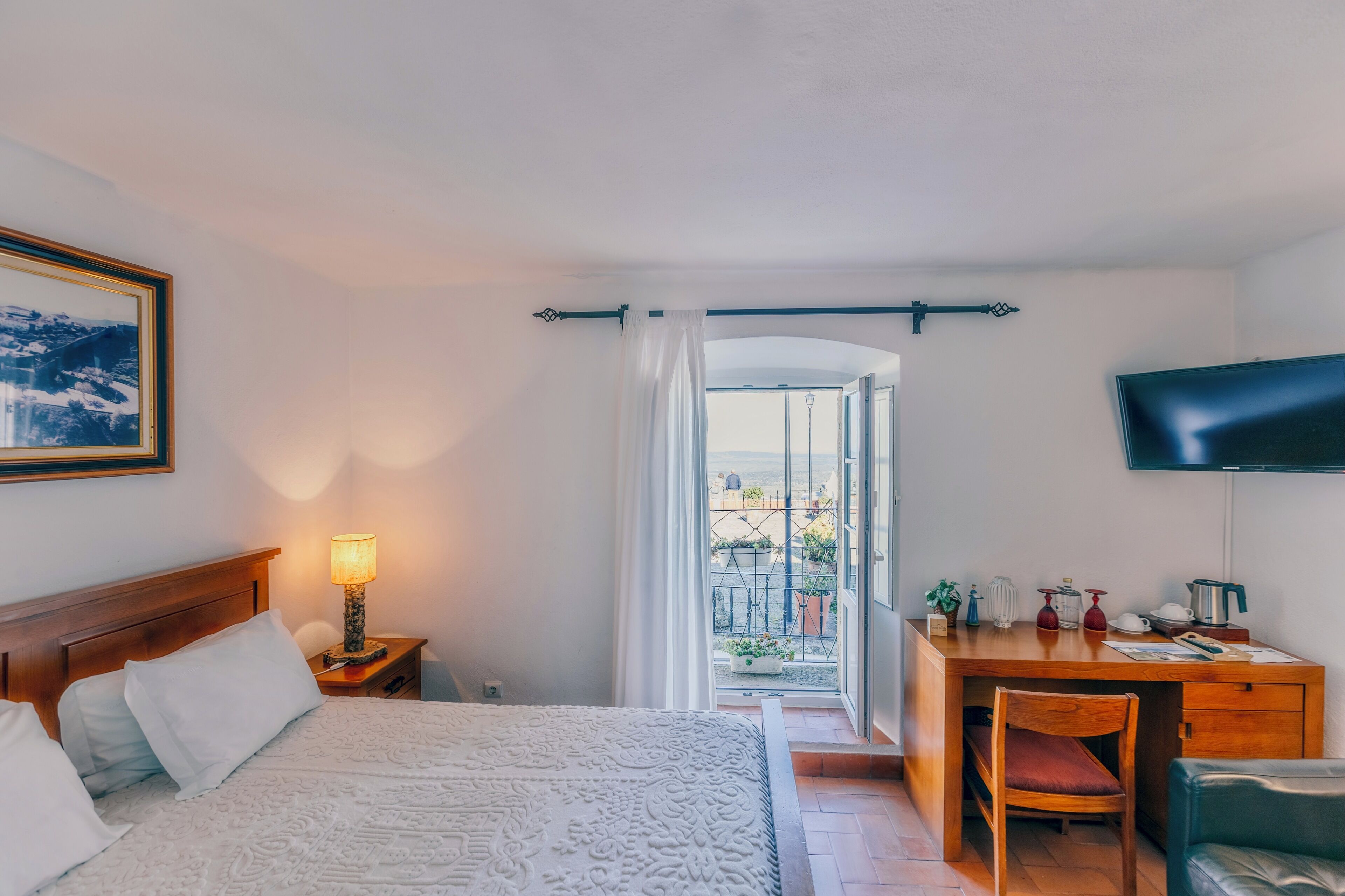 Et hotelværelse med seng, skrivebord, fjernsyn og en balkon med udsigt.