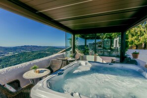Ein Whirlpool auf einem Balkon mit Korbmöbeln und einem Tisch, mit Blick auf eine Berglandschaft.