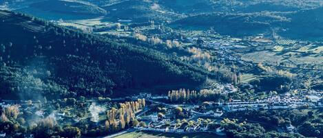Vista aérea de un pueblo con un río, rodeado de colinas y vegetación.