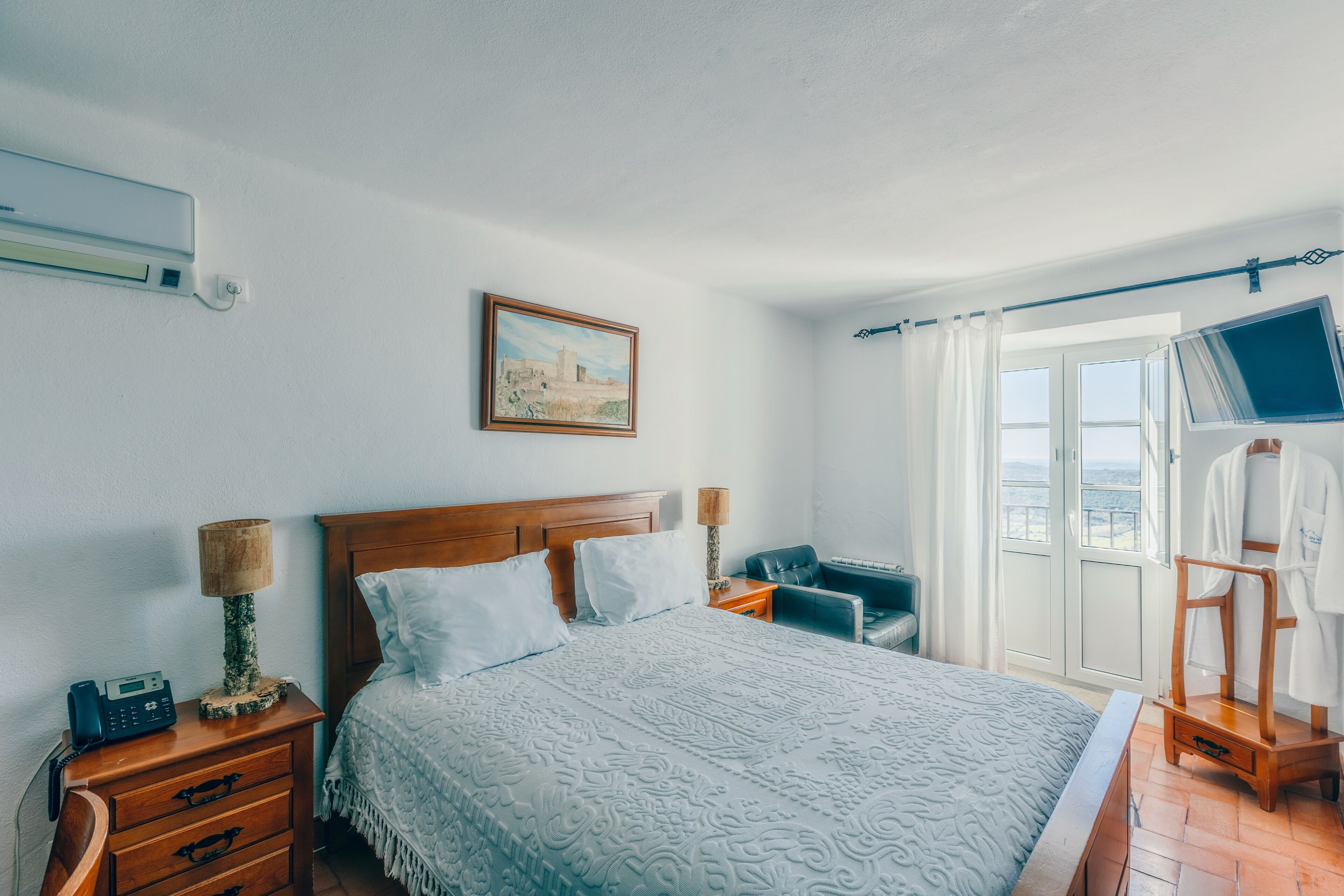 A bedroom with a bed, bedside tables, a chair, a robe stand, a painting, and a window with curtains.